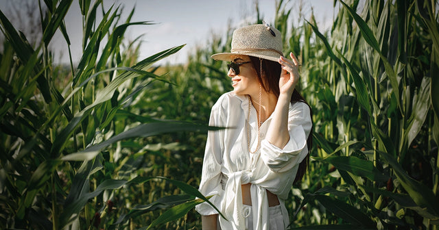 Woman in a white dress and straw hat walking through tall grass