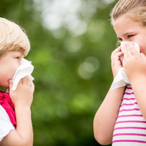 Two young children blowing their noses into tissues outdoors
