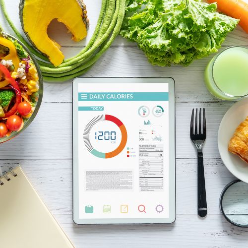 Tablet showing a daily calorie tracker beside fresh vegetables and juice