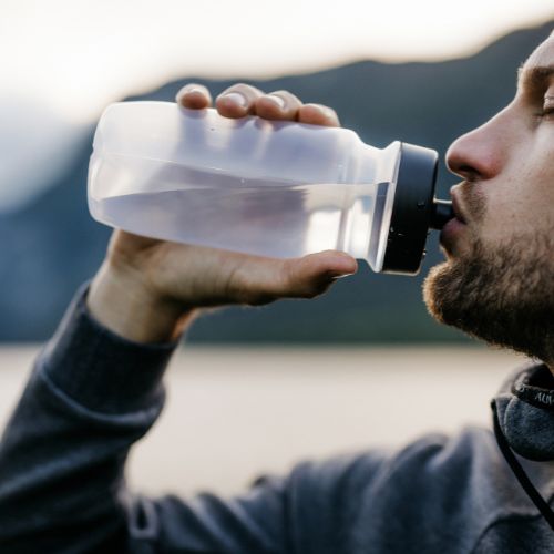 Man drinking from a large water bottle outdoors