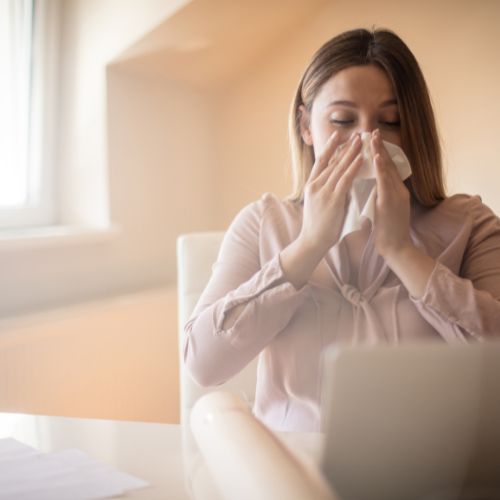 Woman at a desk blowing her nose into a tissue