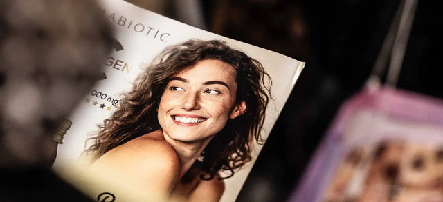 Woman smiling beside Primabiotic Collagen packaging at a beauty show