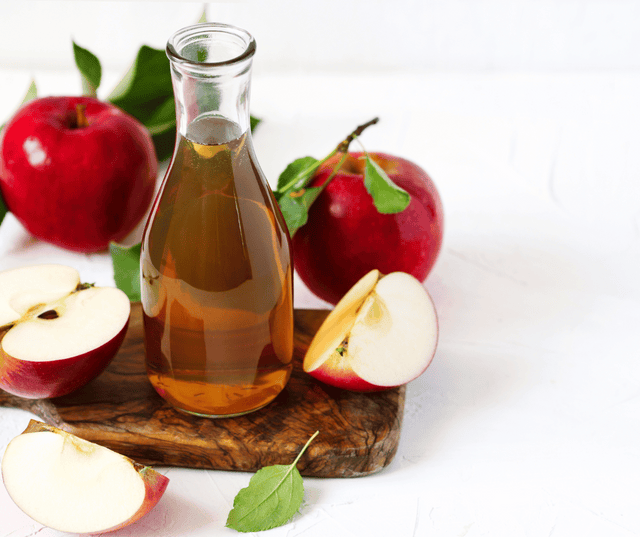 Bottle of apple cider vinegar with fresh apples on a wooden board