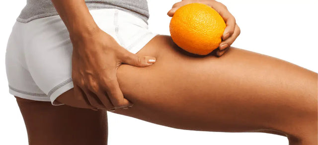 Hand holding an orange against a thigh to illustrate cellulite