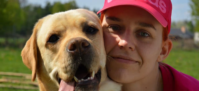 Person in a pink cap hugging a golden labrador in a field