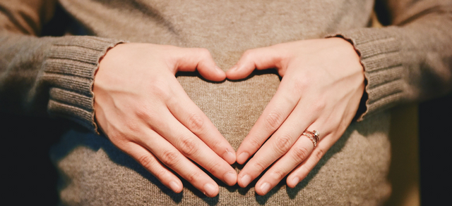 Pregnant woman making a heart shape with her hands over her bump