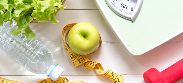 Water bottle, apple, tape measure and scales on a white table