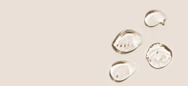 Droplets of clear hyaluronic acid serum on a beige surface
