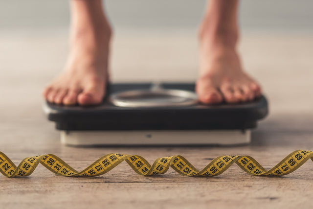 Bare feet on bathroom scales beside a tape measure