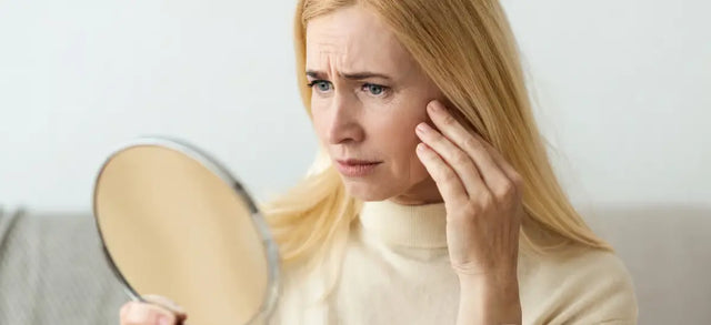 Woman frowning at her reflection in a hand mirror
