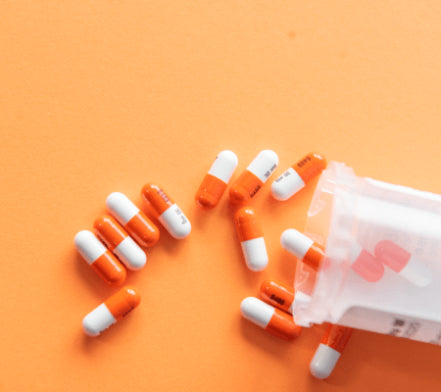 Orange and white capsules spilling from a pill bottle on an orange background