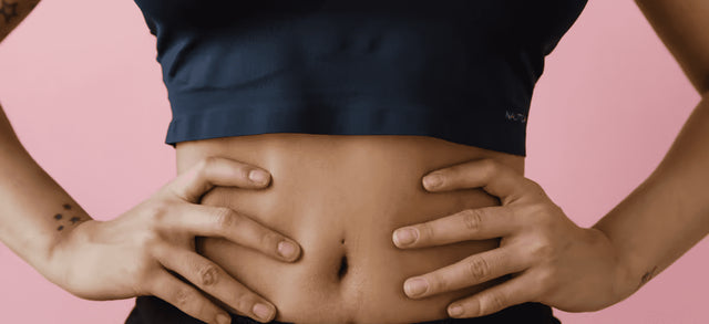 Hands resting on a bare stomach against a pink background