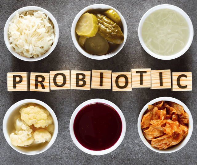 Bowls of sauerkraut, pickles, kefir and kimchi around tiles spelling PROBIOTIC
