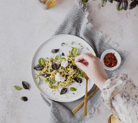 Hand seasoning a plate of salad on a grey cloth