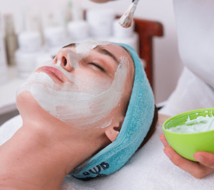 Woman having a white clay face mask applied at a salon