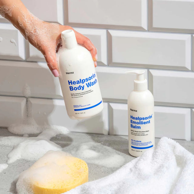 Hand holding Healpsorin Body Wash and Emollient Balm beside a bath sponge