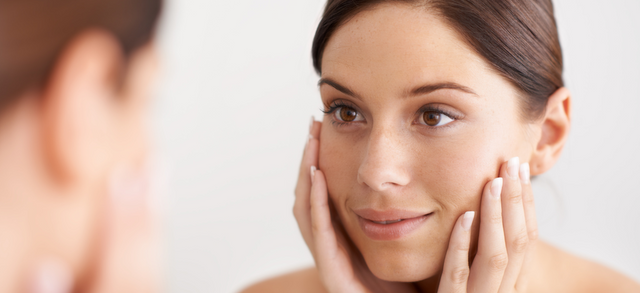 Woman touching her cheeks while looking in a mirror